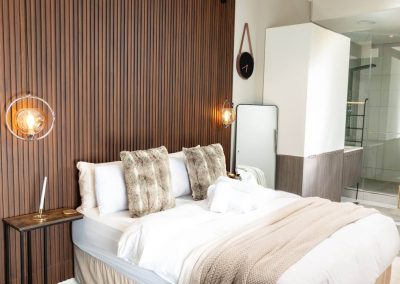Menlyn Maine bedroom interior with fur pillows, wood-panel feature wall, and soft lighting