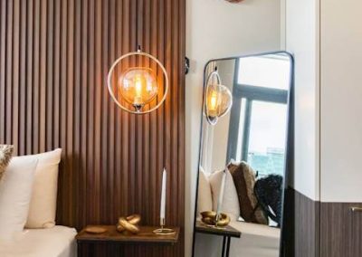 Modern bedroom at Menlyn Maine luxury apartment with wood paneling, stylish lighting, and floor mirror